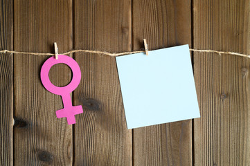 female symbol cut out of paper and blank sticky note attached with a clothespin to a rope on a wooden background. the concept of gender equality. space for text