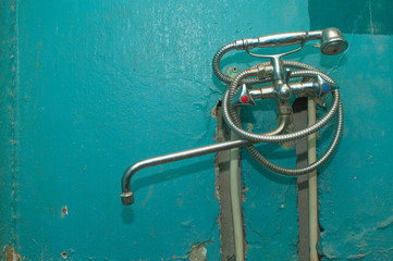 Stainless steel faucet for the bathroom on the background of a green ruined wall. A close-up photo in the repair process.