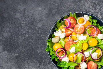 Red yellow cherry tomatoes, goat cheese, onion green salad on dark background. Top view, space for text.