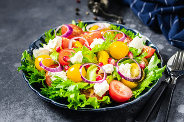 Red yellow cherry tomatoes, goat cheese, onion, pomegranate green salad on dark background. Selective focus, space for text.