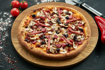 Pizza with a large number of toppings: hunting sausages, onions, mushrooms, salami, cheese and bell pepper. Pizza in composition with ingredients on a black background