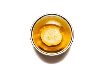 Single Golden Yellow Zucchini silce in a stainless steel bowl, isolated on a white background.