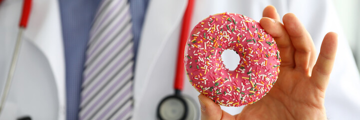 Doctor in office holding in hand pink doughnut