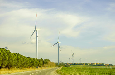 Suburban landscape. Windmills rise above small houses with red tiled roofs. Sunny summer day. Blue...