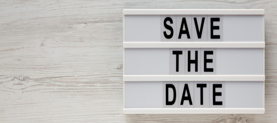 'Save the date' words on a modern board on a white wooden background, top view. Overhead, from above, flat lay. Space for text.