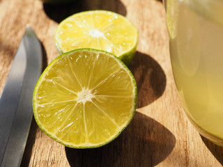  Close up fresh limes sliced in half on a wooden table with a knife and glass, High Vitamin C,...