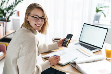 Photo of woman making notes in exercise book and using cellphone