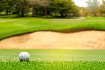 White Golf ball on green course to be shot on blurred beautiful landscape of golf course in bright...