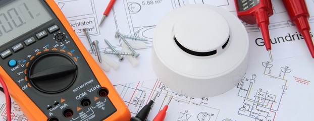 smoke detector with a screwdriver and a measuring device on a circuit diagram