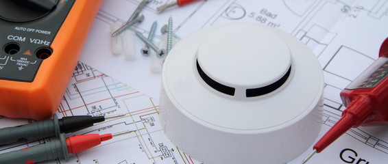 smoke detector with a screwdriver and a measuring device on a circuit diagram