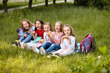 Fototapeta premium Young school kids eating lunch talking, together, sitting on the ground