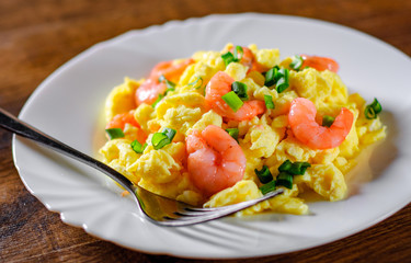 scrambled eggs with shrimp and green onions in white plate on wooden table background.