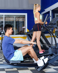 Fototapeta na wymiar Young fitness man and woman doing cardio workout on fitness machines at gym