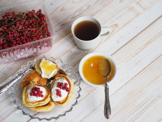 Fritters with sour cream and red currants. Therapeutic tea for colds with honey on a wooden white rustic table. Home kitchen.