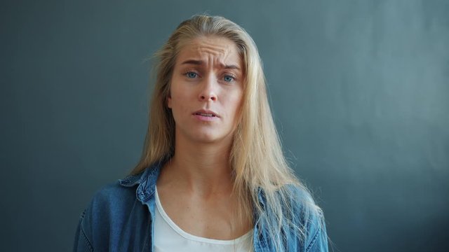 Unhappy young lady is yelling gesturing flapping arms looking at camera feeling sad standing on black background alone. Human emotions and conflict concept.
