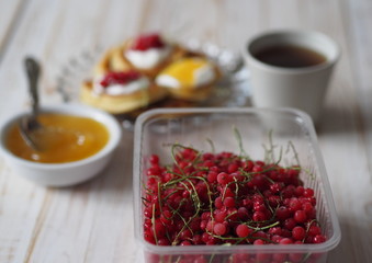Fritters with sour cream and red currants. Therapeutic tea for colds with honey on a wooden white rustic table. Home kitchen.