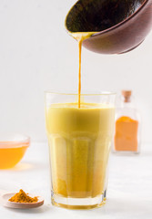 Golden milk with turmeric is poured from a bowl into a glass. on white background. traditional cuisine