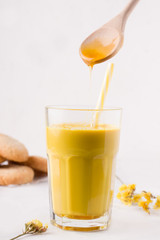 golden milk in which honey is poured from a wooden spoon. healthy drinks