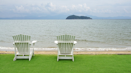White timber seating on the green grass with beach and ocean background