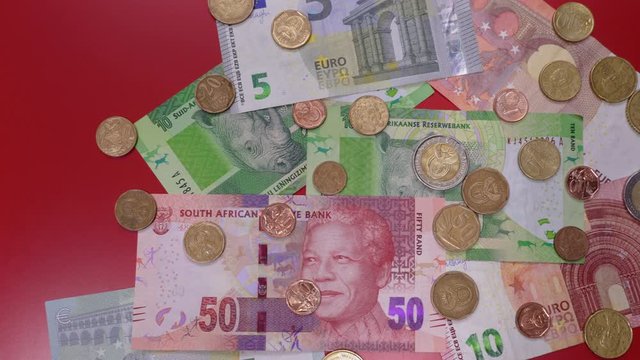 South Africa rand money & coins with euro banknotes top view. ZAR official currency in denominations of 10 & 50 bills with bimetallic cent coins on table next to 5 & 10 euro bills and coins.