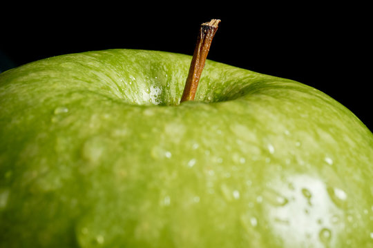 Close up of green apple with water drops on black background