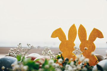 Happy Easter. Stylish easter eggs, yellow bunny in nest of spring flowers on rustic wooden table, space for text. Natural dyed easter eggs and rabbit decorations in light