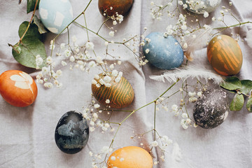 Stylish easter eggs on rustic table flat lay. Natural dyed colorful easter eggs with spring white flowers and feathers on rural textile background. Happy Easter.