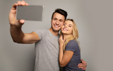 Say “cheese”! Close-up photo of a young blonde girl and a handsome man in casual outfits, who are hugging while making a joint selfie.