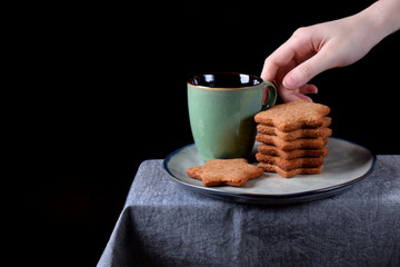 Gingerbread star cookies and a green cup of hot drink on the ceramic plate on the edge of the table...