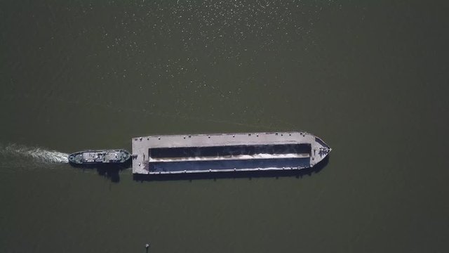 A tugboat ship pushes a barge upstream of the river to transport bulk materials. Aerial photography with a quadcopter or a drone. Panorama of the Dnieper - the main water transport artery of Ukraine