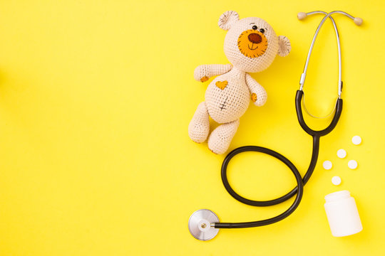 Children's toy teddy bear amigurumi with stethoscope on yellow background with copy space. Child health concept. Top view, flat lay