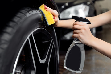 Car wash service, detailing using spray and sponge to wipe black tire