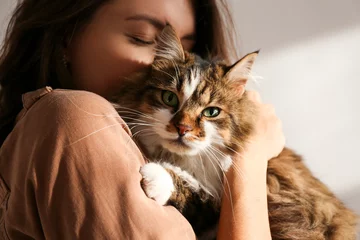 Wall murals Veterinarians Portrait of young woman holding cute siberian cat with green eyes. Female hugging her cute long hair kitty. Background, copy space, close up. Adorable domestic pet concept.