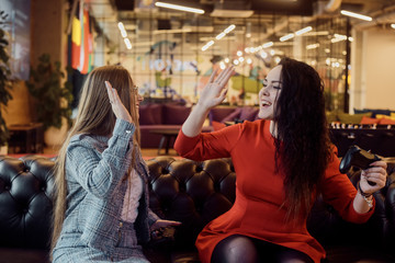 Two girlfriends play video games, holding joysticks in their hands. Console games, addiction, streamers. The girls won the video game, give five, laugh. Female power, victory, joy.