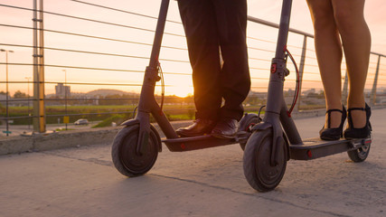 LOW ANGLE: Business partners in formal wear ride e-scooters to work at sunrise.