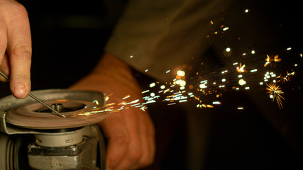 CLOSE UP, DOF: Sparks fly off spinning angle grinder grinding a piece of metal.