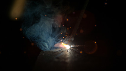 MACRO, DOF: Weld created by unrecognizable metalworker glows in a dark workshop. - obrazy, fototapety, plakaty