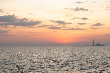 Naklejka na ściany i meble The red sun over the evening sea near the industrial area by the sea