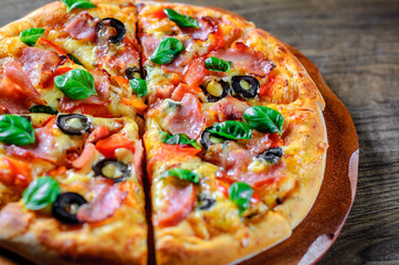 Pizza with Mozzarella cheese, ham, pepper, olive, meat, Tomato sauce, Spices and Fresh Basil. Italian pizza on wooden background