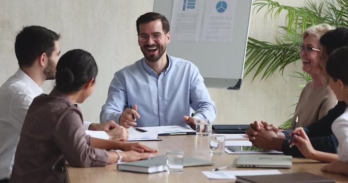 Cheerful diverse business team talking laughing at meeting table