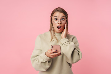 Portrait of young shocked woman using cellphone and looking at camera