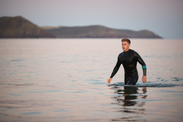 Man Wearing Wetsuit Wading Through Shallow Sea By Shore