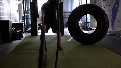 Man working out at the gym using battle ropes to workout his upper body.