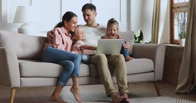 Family of four hugging making videocall on laptop on sofa