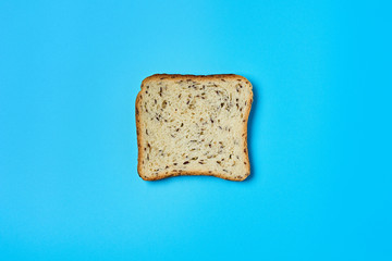 Single square piece of bread with seeds for toast lies on blue table on kitchen. Top view. Close-up