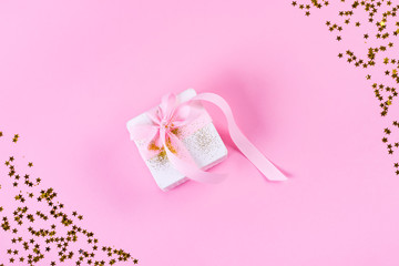 Gift or present box with confetti stars and pink ribbon on pastel pink background. Holiday pattern. Flat lay style.