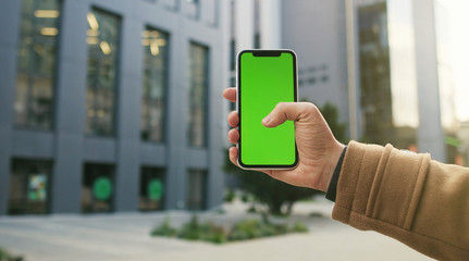Cropped shot view of  male hand holding smart phone on on city street background with blank copy space screen for your text message or information content