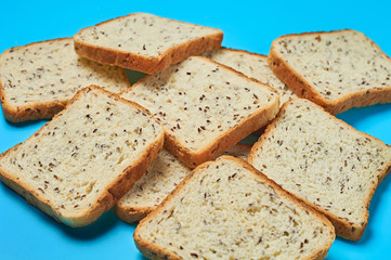 Heap of square pieces of bread with seeds for toast lies on blue table on kitchen. Close-up
