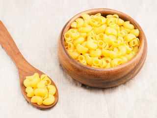 Pasta helices type in wooden bowl and spoon on a beige fabric background. Healthy eating concept