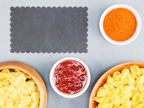 Different Types Of Pasta In Wooden Bowls, Red Chili, Tomato Sauce On A Gray Concrete Background With Copy Space. Healthy Eating Concept